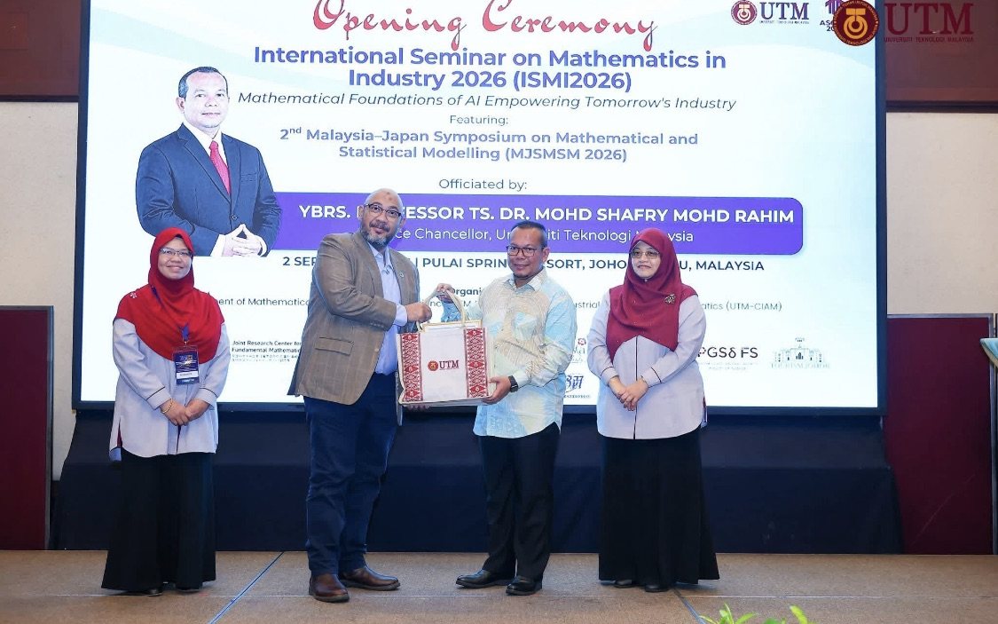 Reza Ali presenting a gift on stage at the opening ceremony of ISMI2026, the International Seminar on Mathematics in Industry, at Pulai Springs Resort in Johor Bahru. The backdrop names the seminar and its Malaysian and Japanese sessions.