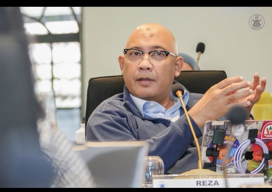 Reza Ali speaking at a roundtable table, gesturing with one hand, with a name card reading REZA in front of him and an ISIS Malaysia watermark in the corner.