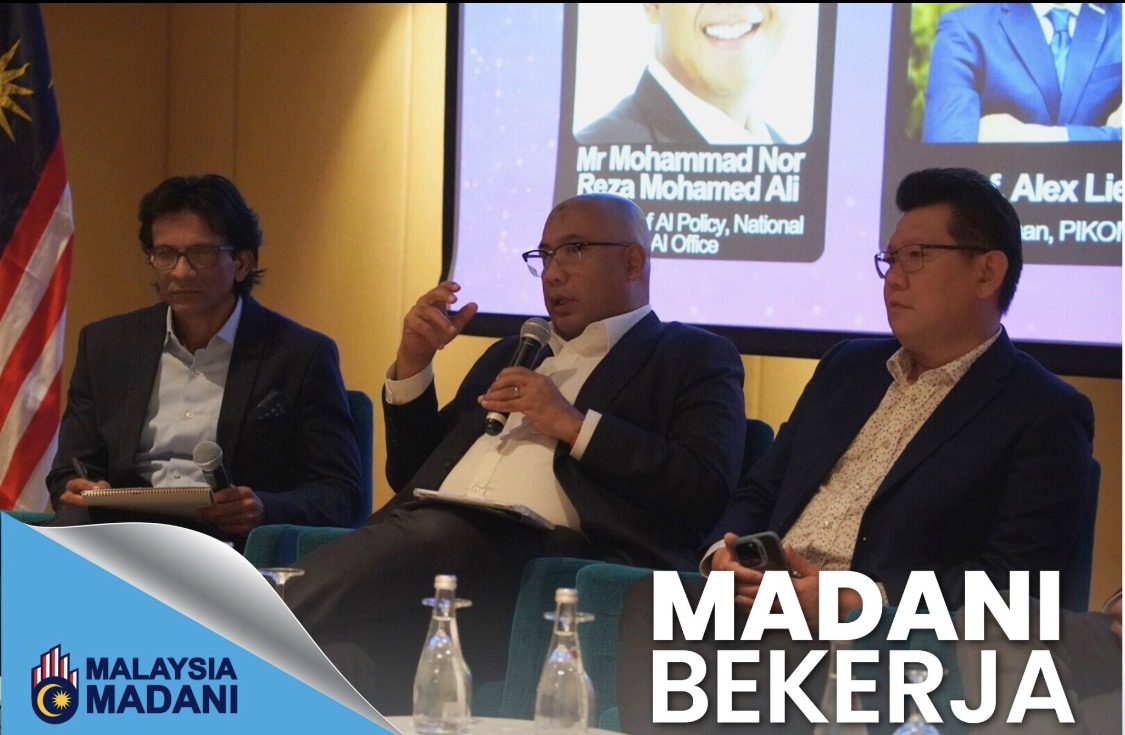 Reza Ali speaking with a microphone on a panel at the Malaysia–India Conclave, with a slide behind listing the panellists, including the Director of AI Policy, National AI Office, and the Chairman of PIKOM