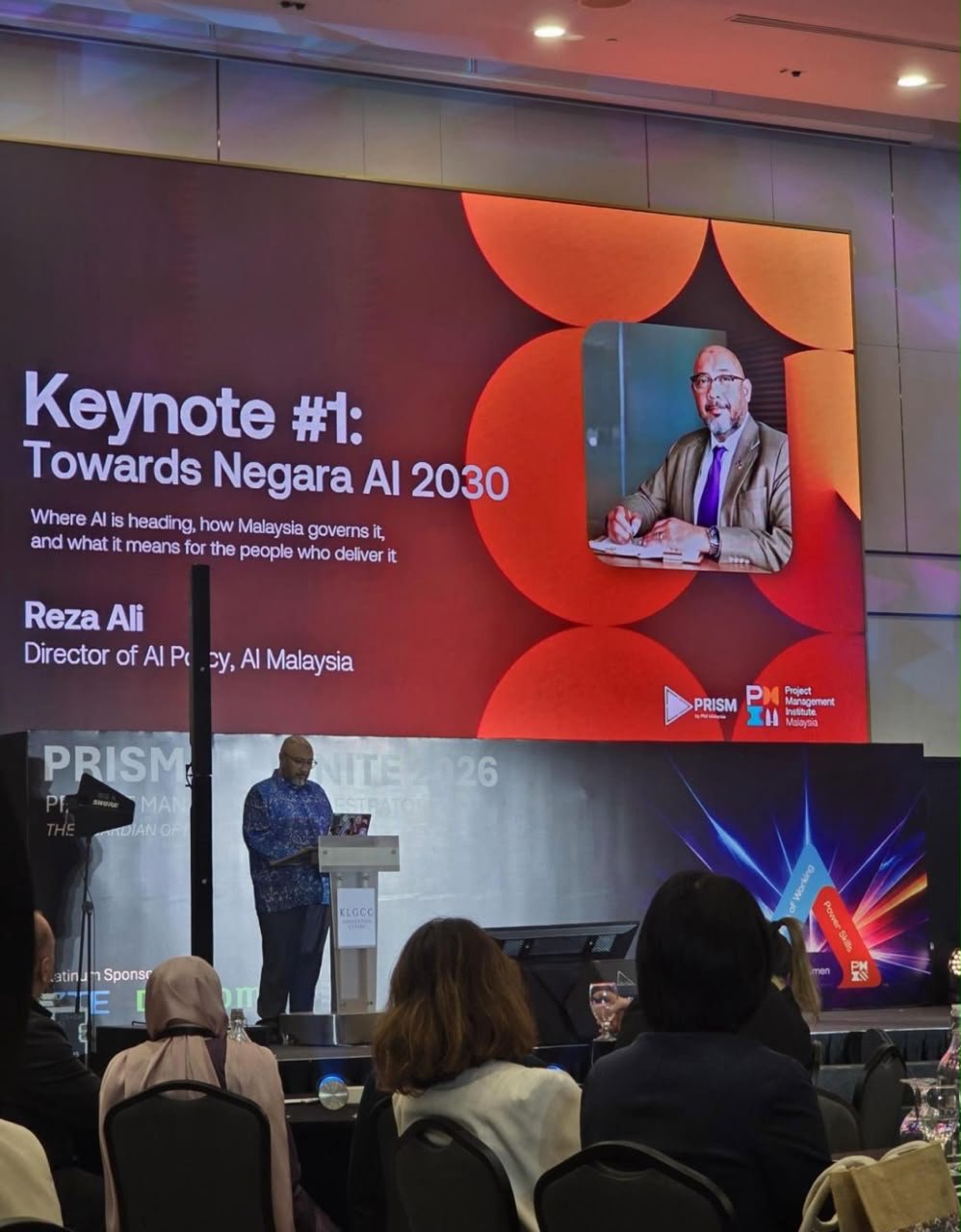 Reza Ali delivering Keynote #1, Towards Negara AI 2030, at PRISM & IGNITE 2026, KLGCC, with the keynote slide on screen